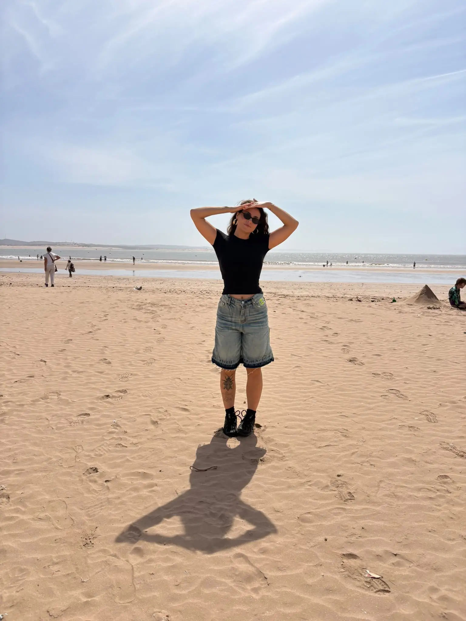 Amalia en una playa enorme, con gafas de sol y las manos sobre la cabeza