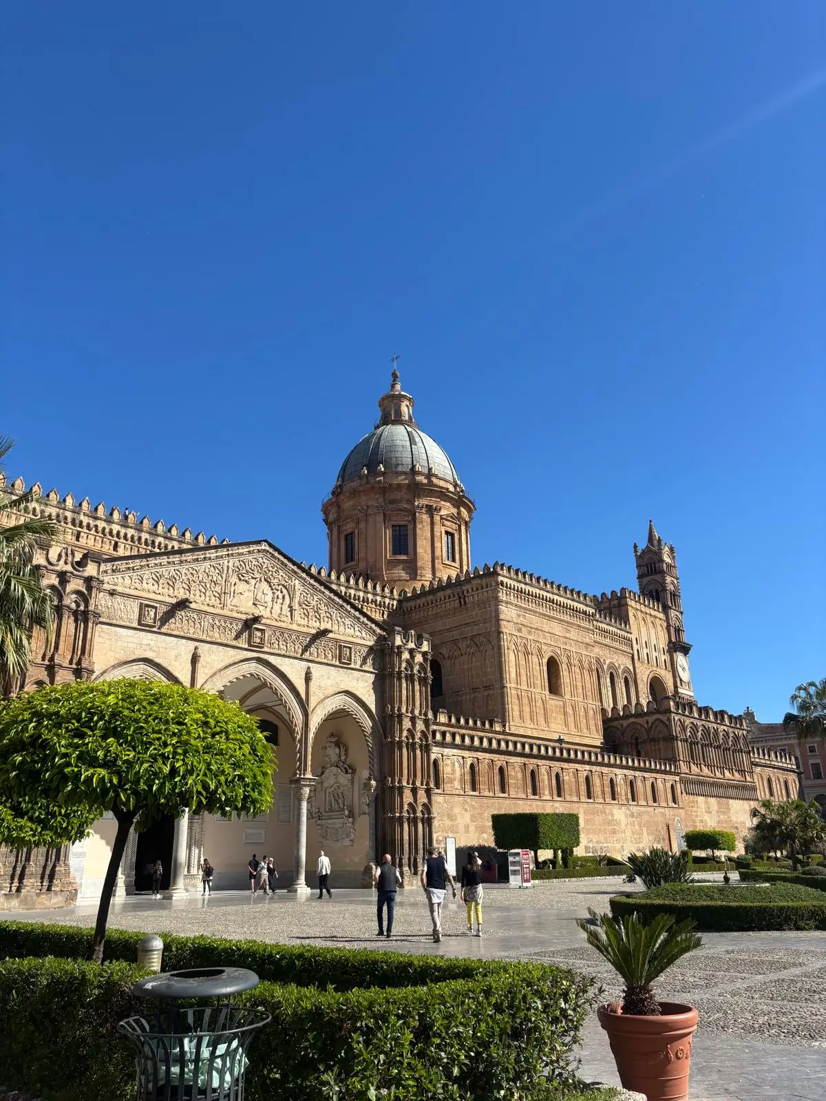 La catedral de Palermo, en Sicilia, con su cúpula bajo un cielo azul y jardines delante